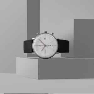 Close-up view of a Junghans Max Bill Chronograph wristwatch featuring a minimalist design, with a white dial, simple black hour markers, and a slender black leather strap